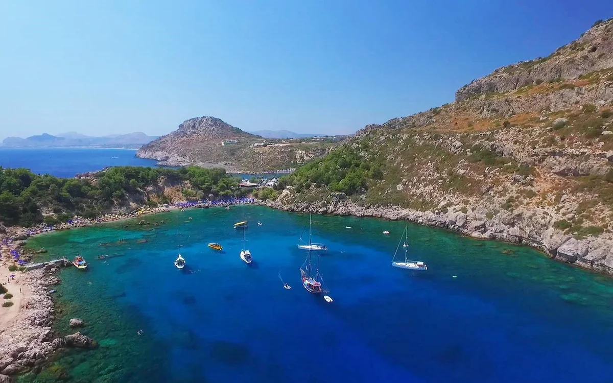 A deep blue bay ringed by rocky hills seen from above, with small boats anchored in the middle of it