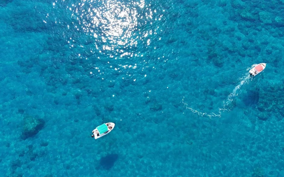 A single small white boat under way on open blue water off the coast of Rhodes, seen from high above