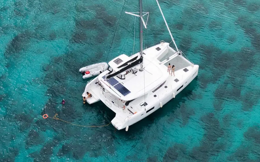 An aerial view of a white catamaran on clear turquoise water with a swimmer in the water beside it