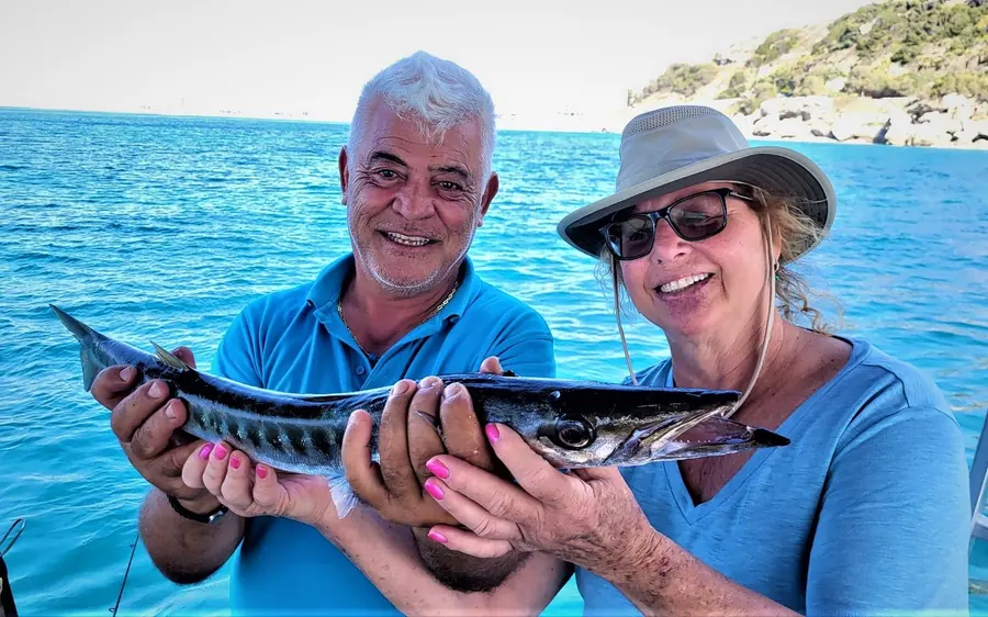 A man and a woman on a boat deck holding up a freshly caught fish between them
