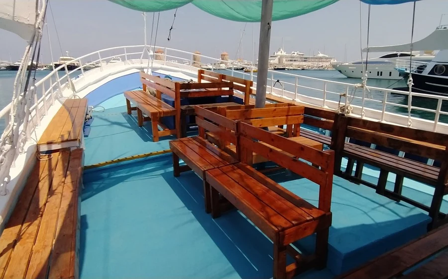 Wooden benches and tables under a canopy on the deck of a traditional boat moored in a harbour