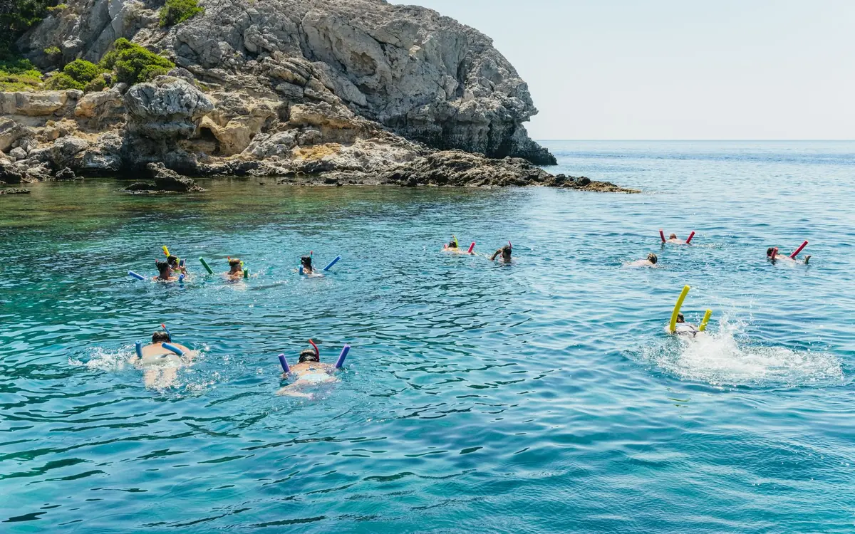 A dozen people swimming in clear water off a rocky headland on the east coast of Rhodes